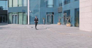 Takım elbiseli kendine güvenen bir işadamı açık havada elektrikli scooter kullanıyor.