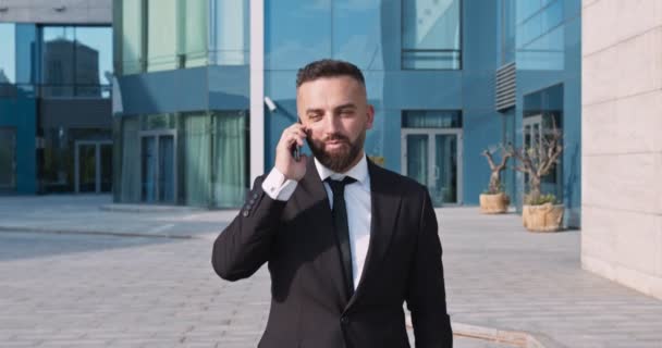 Biznesmen w garniturze przechodzi dalej i omawia projekt z partnerami przez telefon komórkowy — Wideo stockowe