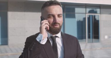 Ofis binasının önünde cep telefonuyla konuşan başarılı iş adamının görüntüsü.