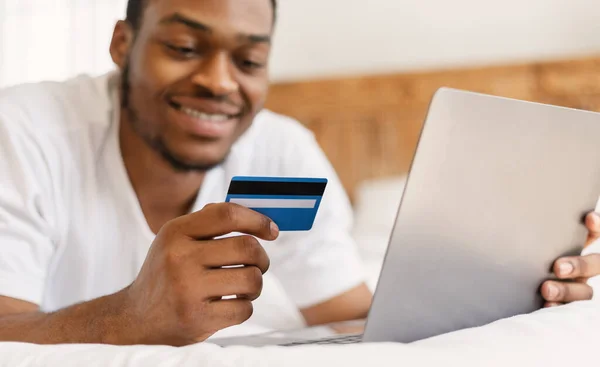Hombre negro haciendo compras en línea acostado en la cama en casa —  Fotos de Stock