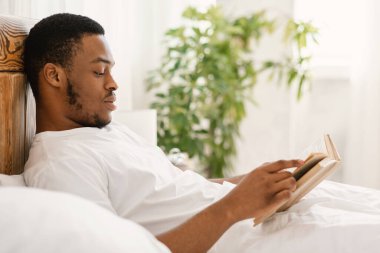 Siyah adam kitap okuyor. Yatak odasında uzanıyor.