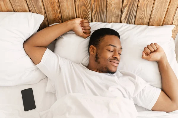 非洲男人躺在舒适的卧室里舒展着双手醒来 — 图库照片