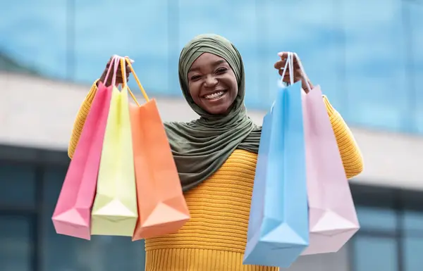 Açık havada poz veren bir sürü alışveriş çantasıyla mutlu siyah Müslüman kadın. — Stok fotoğraf