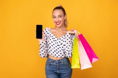 Mutlu kadın siyah telefon ekranı ve alışveriş torbaları gösteriyor.