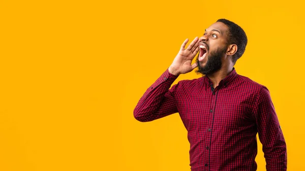 Tipo negro cogido de la mano cerca de la boca, gritando a un lado en copyspace — Foto de Stock