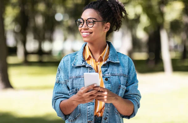 Afrikanska student flicka med mobiltelefon promenader på helgen i parken — Stockfoto