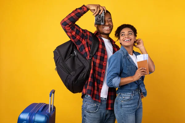 Turistas africanos con cámara y equipaje de pie sobre fondo amarillo — Foto de Stock