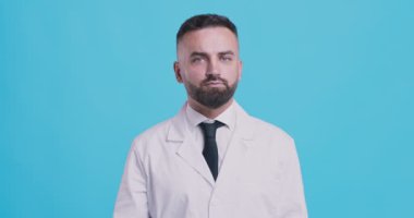 Sosyal uzaklık kavramı. Ciddi bir tıp doktoru kafasını sallıyor ve işaret ediyor, mavi arka plan.