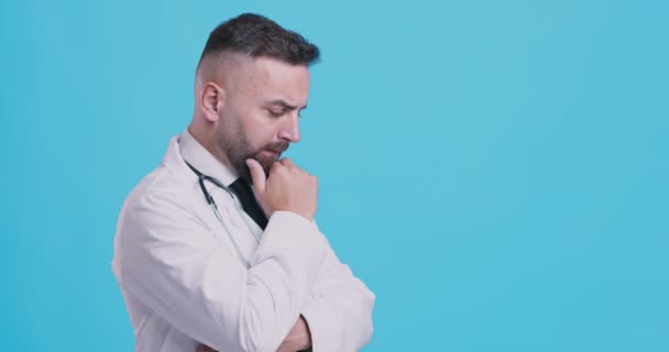 Dokter dewasa berpikir tentang situasi pasien, latar belakang studio biru, tampilan samping, ruang kosong — Stok Video