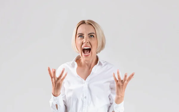 Beautiful blonde businesswoman in office wear shouting in anger on light studio background — Stock Photo, Image