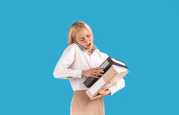 Segretario donna stressata con un mucchio di documenti che parlano su smartphone su sfondo blu studio — Foto Stock