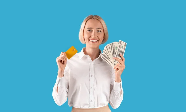 Retrato de mulher de negócios feliz segurando dinheiro e cartão de crédito sobre fundo estúdio azul, panorama — Fotografia de Stock