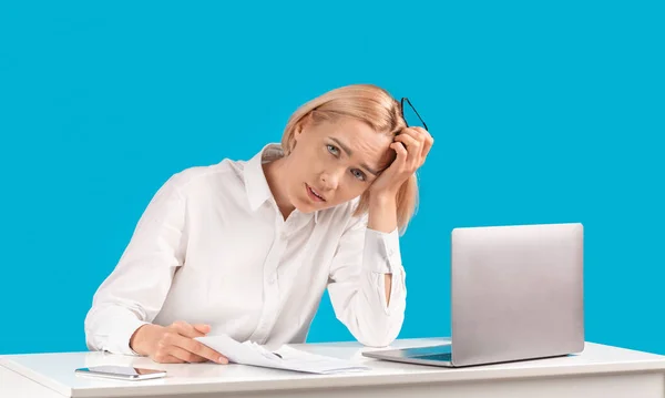 Atraktivní podnikatelka unavená z počítačové práce sedí u svého stolu nad modrým studiem pozadí, panorama — Stock fotografie