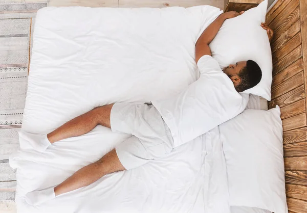 Irreconocible negro chico durmiendo acostado en el estómago en cama interior —  Fotos de Stock