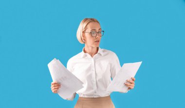 Resmi kıyafetler ve gözlüklü ciddi bir iş kadını portresi mavi stüdyo arka planında dokümanlar taşıyor.