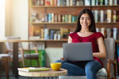Mobil Ofis. Cafe 'de dizüstü bilgisayarla oturan neşeli Asyalı Serbest Kadın