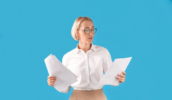 Porträt einer seriösen Geschäftsfrau in formeller Kleidung und Brille mit Dokumenten vor blauem Studiohintergrund — Stockfoto