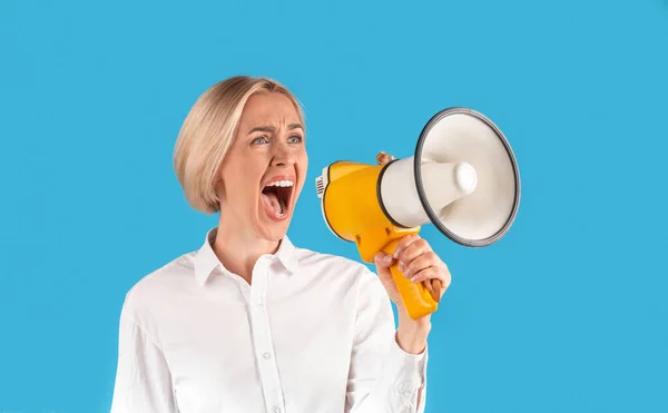 Aufgewühlte blonde Frau in offizieller Kleidung ruft in Megafon auf blauem Studiohintergrund, Panorama — Stockfoto