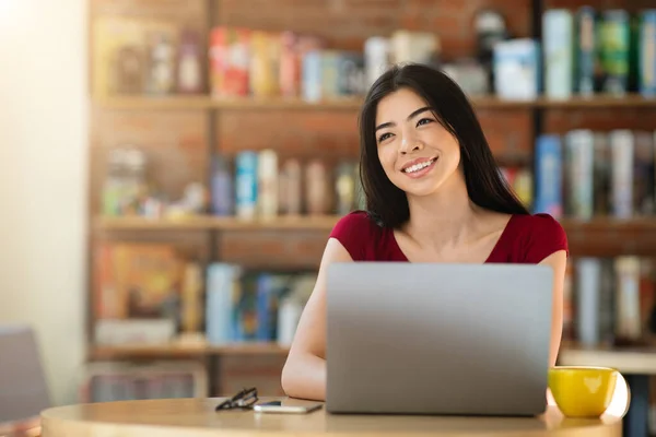 Asiatische Frau träumt von etwas, während sie an Laptop in Cafe Bar arbeitet — Stockfoto