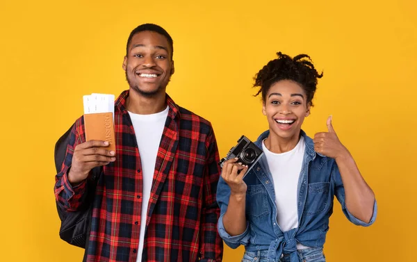 Couple afro-américain tenant billets d'avion et caméra, fond jaune — Photo
