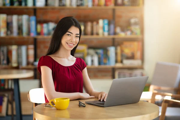 Alegre asiático mujer trabajando remotamente en el ordenador portátil en café, sonriendo en cámara —  Fotos de Stock