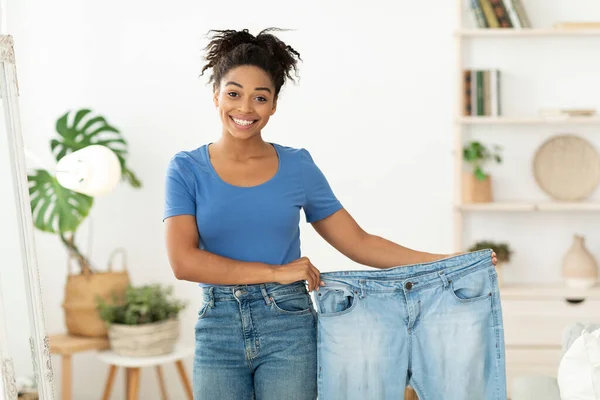 Felice sottile nero donna mostrando vecchi jeans in piedi a casa — Foto Stock