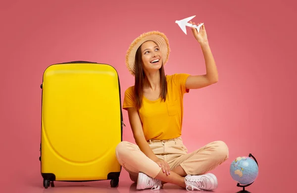 Šťastná dáma si hraje s papírovým letadlem, sedí vedle kufříku — Stock fotografie