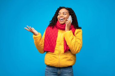 Neşeli siyahi kadın cep telefonuyla konuşuyor Mavi arka planda duruyor