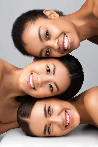 Três mulheres diferentes posando juntas sorrindo em fundo cinza, vertical — Fotografia de Stock