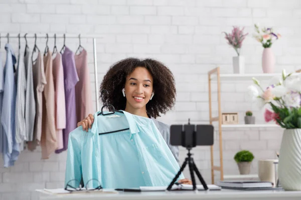 Kleding op afstand adverteren tijdens quarantaine. glimlachende vrouw in draadloze hoofdtelefoon maakt video voor blog op webcam — Stockfoto