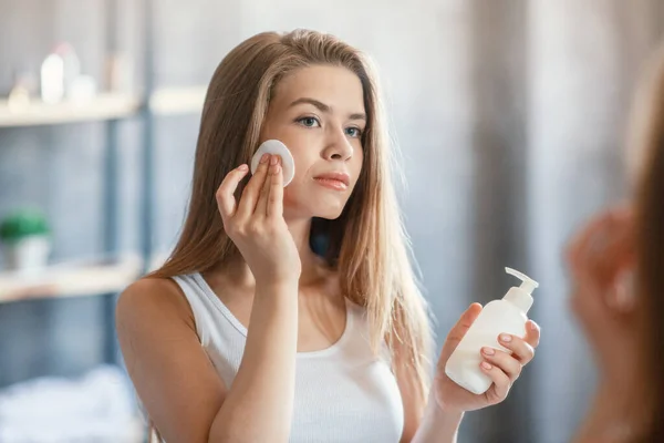 Wanita cantik menggunakan tonik wajah atau make up remover di depan cermin di kamar mandi — Stok Foto