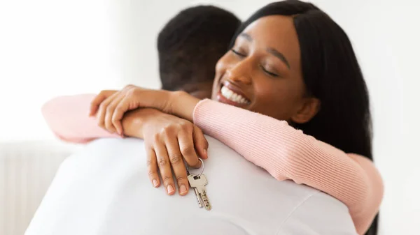 Gülümseyen siyah kadın elinde yeni evin anahtarı ve içeride kocasına sarılıyor. — Stok fotoğraf