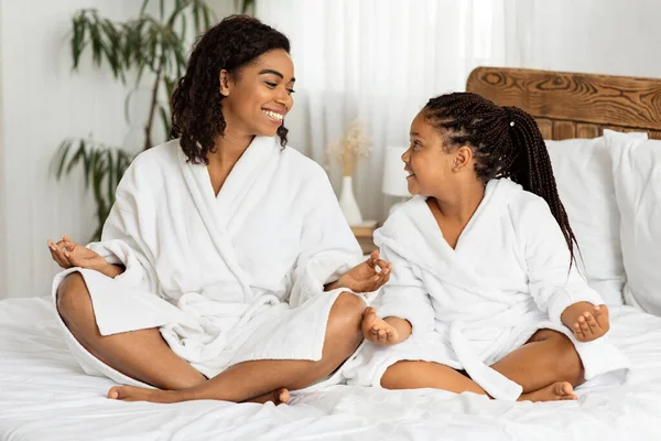 Yoga en familia. Feliz negro mamá y hija usando batas de baño meditando juntos — Foto de Stock