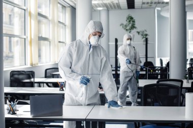 Tehlikeli maddeler, koruyucu maske ve gözlüklü insanlar Coronavirus karantinası sırasında kimyasallarla mobilyaları dezenfekte ediyorlar.