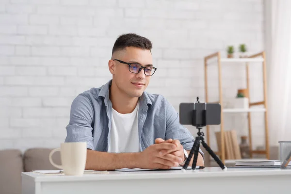 Blogueur moderne ou enseignant travaille de la maison. Jeune homme regardant webcam, blog d'enregistrement ou webinaire, utilise un smartphone avec trépied à l'intérieur du salon — Photo