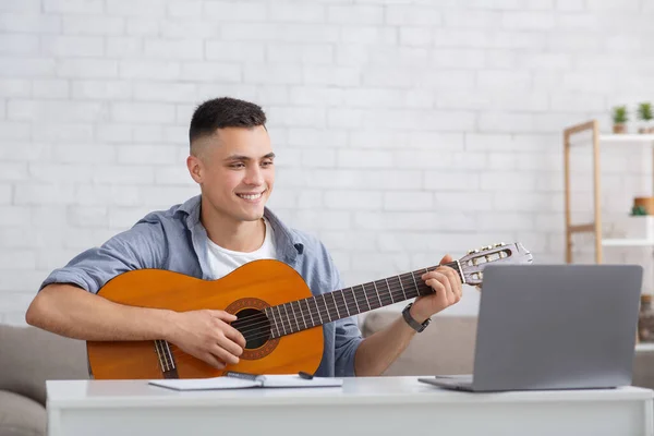 Lezione di musica online a casa e nel tempo libero durante l'epidemia di COVID-19. Felice ragazzo con chitarra guarda laptop e studi — Foto Stock