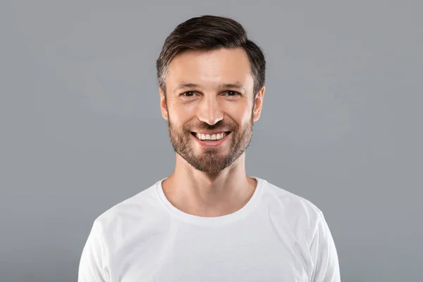 Красивий молодий білий чоловік посміхається на камеру на сірому — стокове фото