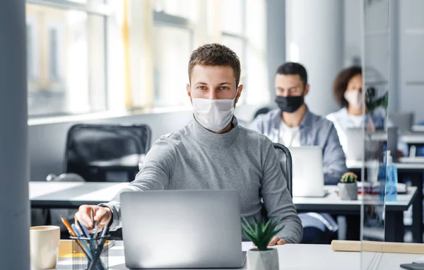 Trabalhador atraente no local de trabalho leva lápis em suas mãos atrás do laptop. Cara em máscara protetora senta-se à mesa no interior do escritório durante a quarentena — Fotografia de Stock