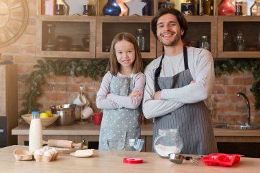 Genç, yakışıklı baba ve küçük kızı mutfakta önlüklü poz veriyorlar.