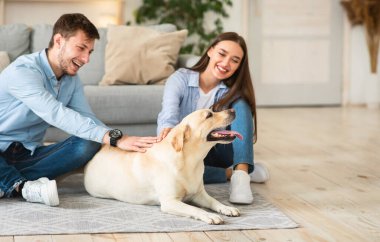 İki kişilik genç bir aile köpeğiyle yerde oturuyor.