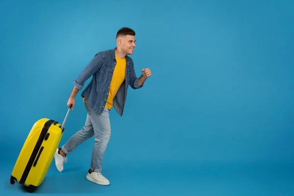 Full length portrait of cheerful male tourist with luggage running towards copy space over blue studio background — Stock Photo, Image