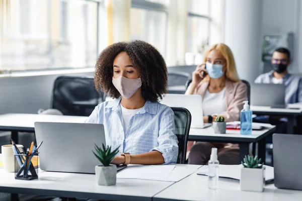 Distanciamento social na situação de surto de coronavírus. Senhora americana muito africana em máscara protetora digitando no laptop, trabalhando para o centro de suporte da empresa — Fotografia de Stock