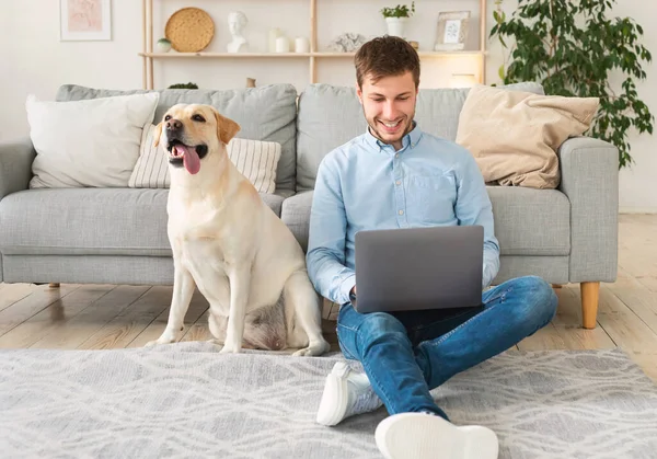 Hombre joven en casa con portátil y mascota feliz — Foto de Stock