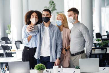 Selfie ya da iş için video çağrısı. Meslektaşlar koruyucu maskeler takıp, akıllı telefona bakıyorlar ve webcam 'de patronla konuşuyorlar.