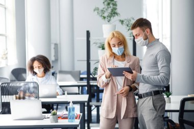 Koruyucu maskeli meslektaşlar projeyi tartışıyor ve birlikte çalışma ofisindeki tablete bakıyorlar