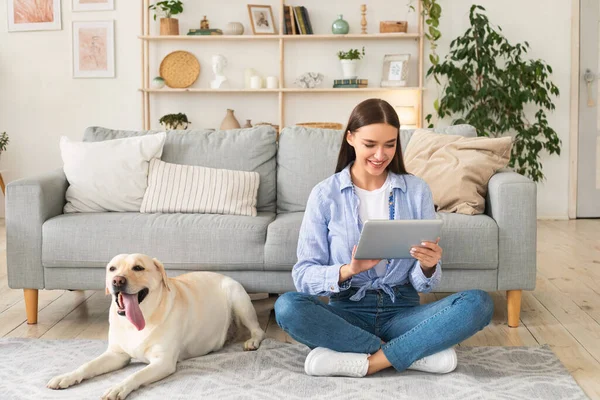 Mujer joven en casa con una tableta y un perro — Foto de Stock