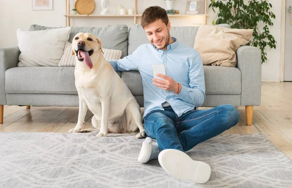 Retrato de un joven con su perro usando el teléfono móvil — Foto de Stock