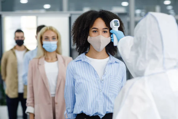 Checking temperature of multiracial workers in protective masks with infrared thermometer in coworking office — Stock Photo, Image