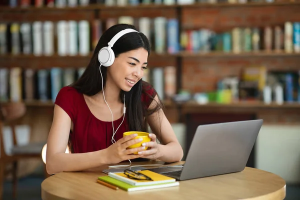 Sonriendo mujer asiática viendo webinar con el ordenador portátil y los auriculares en el café —  Fotos de Stock