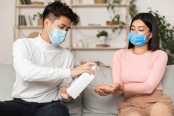 Азиатская пара с помощью дезинфицирующего средства носить защитные медицинские маски, сидя в помещении — стоковое фото
